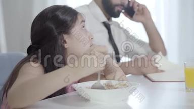 令人沮丧的中东漂亮女孩的肖像，回首看着<strong>无法</strong>辨认的父亲在早餐时打<strong>电话</strong>
